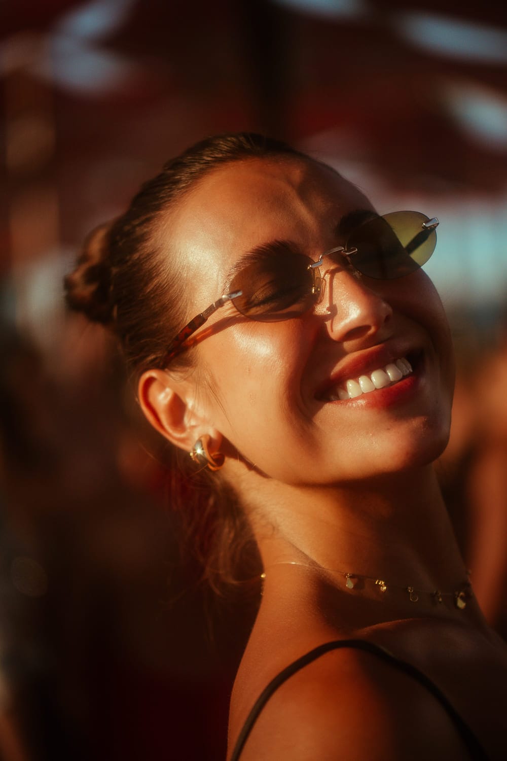 Close de Cristina sorrindo de óculos escuros sob a luz dourada de um dia de praia