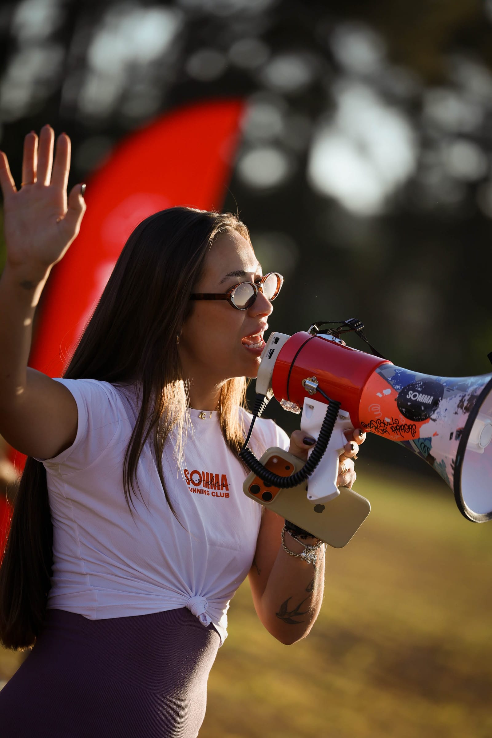 Cristina falando em um megafone com a mão erguida, durante um evento ao ar livre no fim da tarde